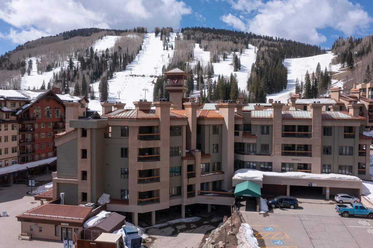 A stunning exterior view showcasing the building's architecture framed by ski slopes and a dramatic mountain backdrop. The warm glow of sunset highlights the potential for cozy evenings and outdoor relaxation after a day of mountain adventures, making it ideal for couples seeking both excitement and serenity.