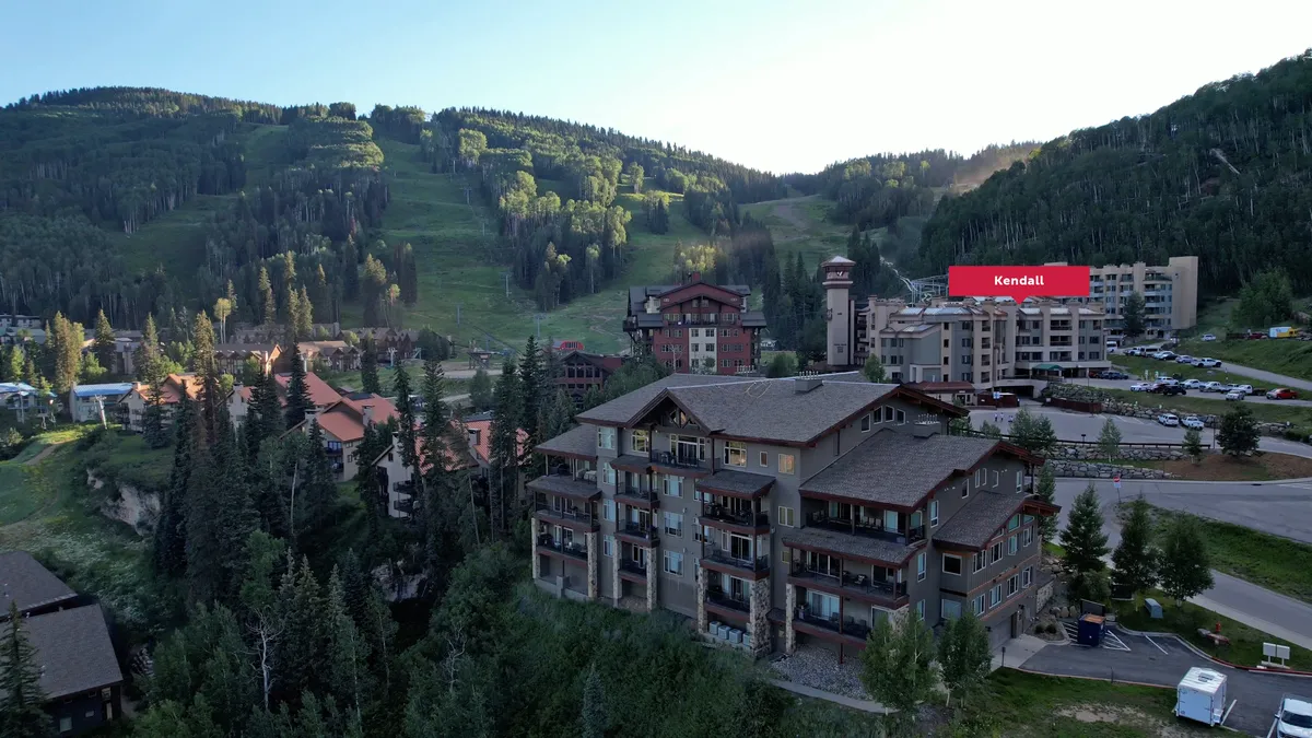 This exterior shot captures the resort buildings nestled among trees with a dramatic mountain backdrop. The parking area is visible, underscoring the convenience of on-site garage parking. The overall mood is serene and adventurous, suggesting opportunities for outdoor fun and relaxation.