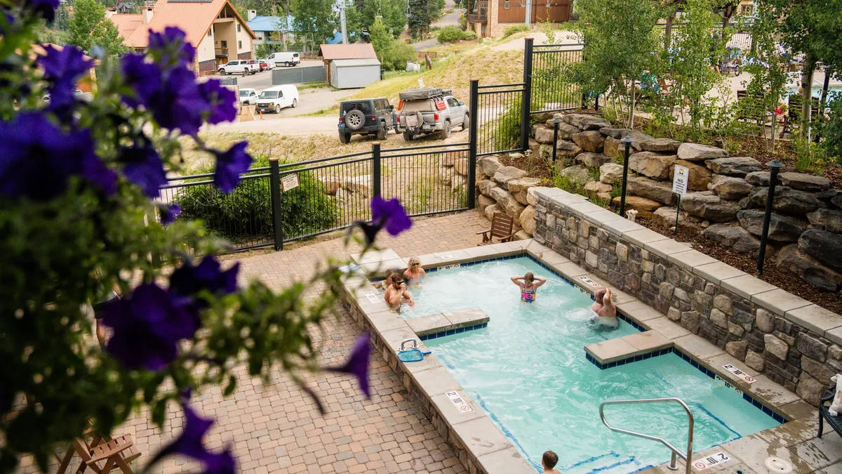 An inviting outdoor heated pool surrounded by vibrant flowers and people enjoying the water. The atmosphere is lively yet relaxing, perfect for social gatherings or unwinding after a day of mountain adventures.