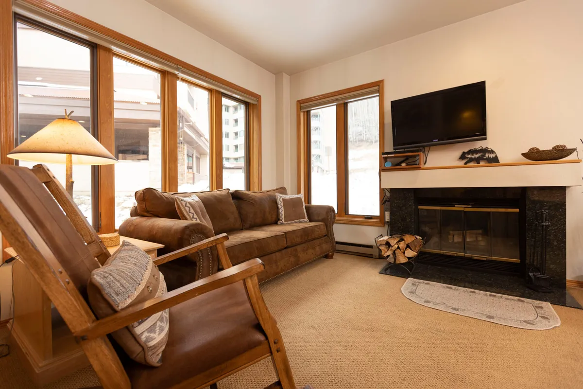 A cozy seating area with a plush sofa set in front of a fireplace, flanked by large windows that offer views of the snowy outdoors. The TV is positioned for group movie nights, while the overall arrangement fosters intimate conversation and unwinding after a day on the slopes.