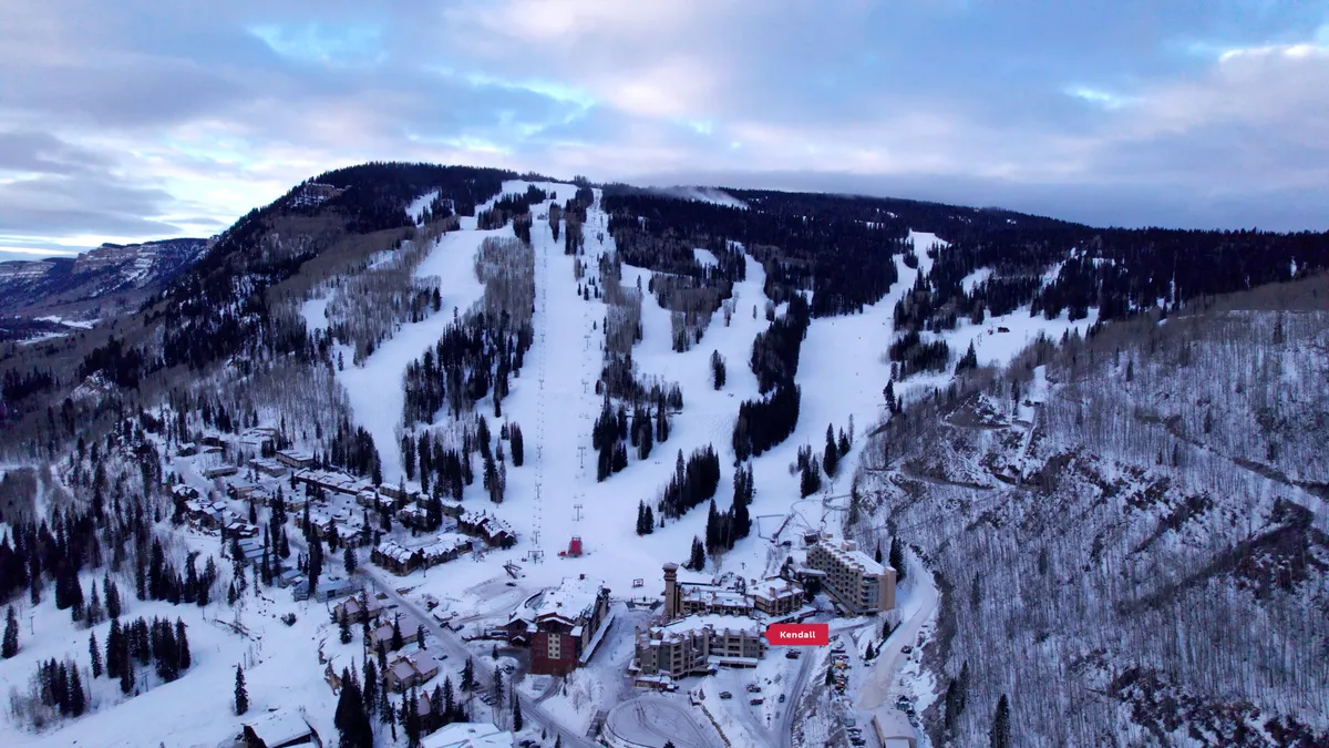 A sweeping view of the ski slopes leading down to the resort buildings, with snow-capped mountains forming a dramatic backdrop. The image captures the thrill of being right on the mountain, showcasing both the accessibility to skiing and the picturesque environment that surrounds the property.