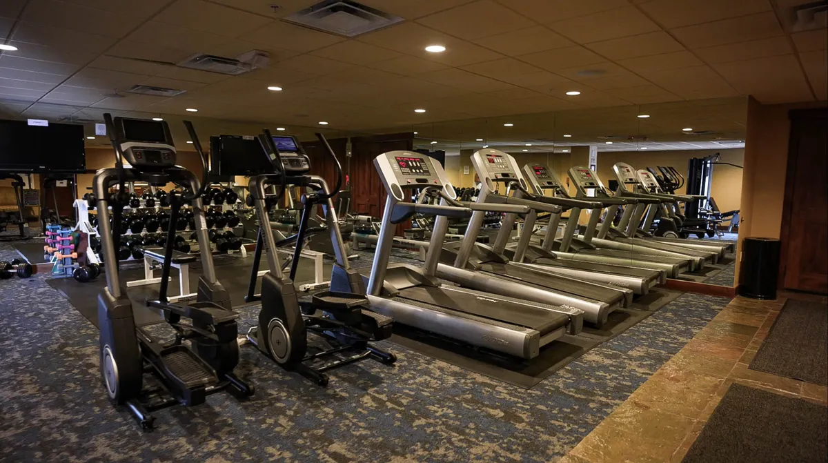 A spacious, well-equipped fitness center featuring treadmills, elliptical machines, dumbbells, and mirrored walls. The environment is bright and motivational, encouraging guests to maintain their workout routines while enjoying resort life.