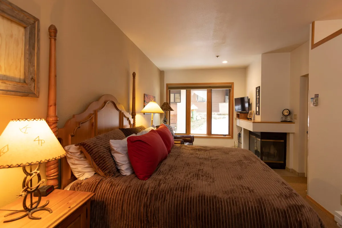 This image displays a spacious master suite featuring a king-sized bed dressed in plush bedding, a cozy fireplace, a window that lets in soft natural light, and warm bedside lamps. The room feels both inviting and luxurious, perfectly capturing the notion of a relaxing retreat.