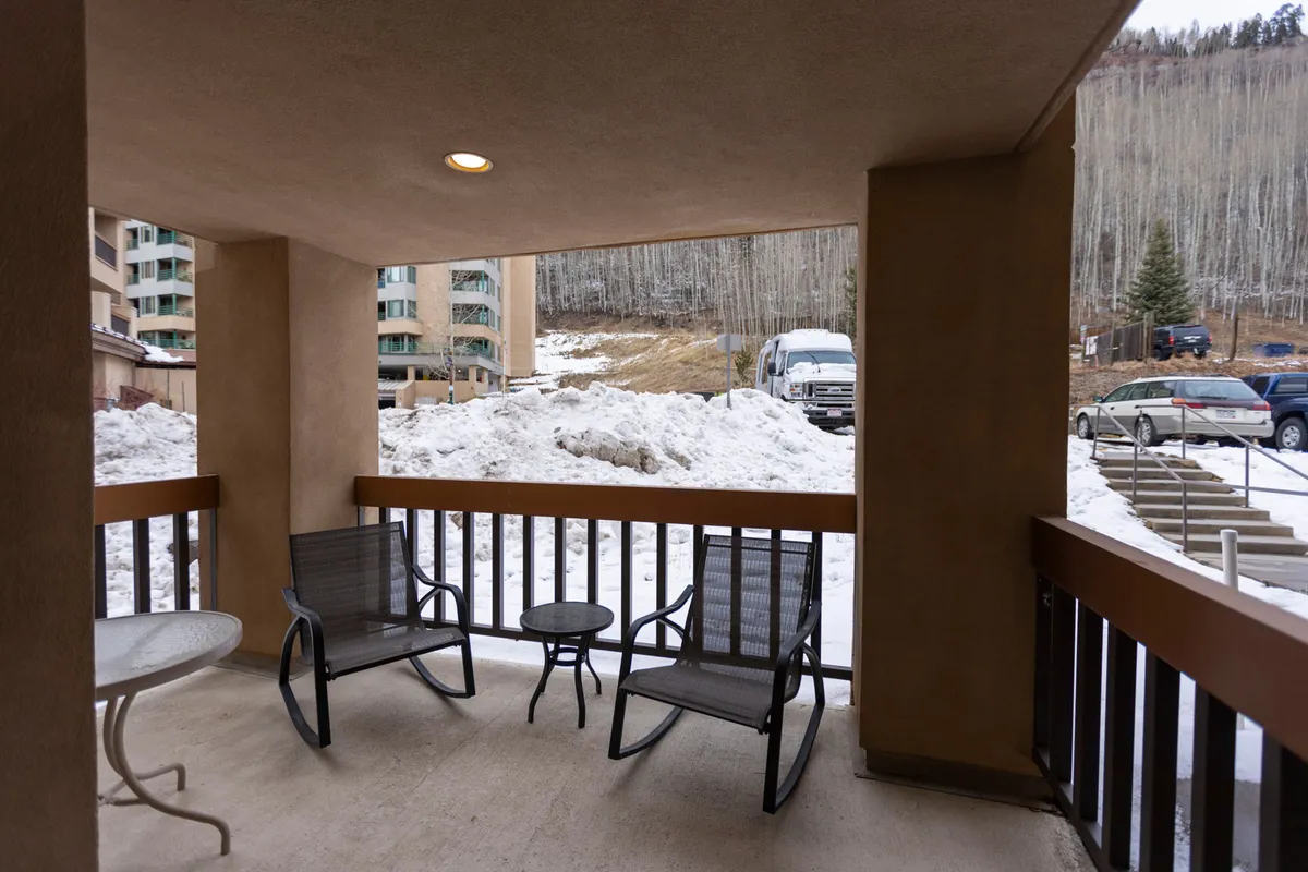 A cozy corner patio with comfortable seating, surrounded by a picturesque snowy landscape and neighboring resort buildings. The scene evokes a sense of tranquility and a close connection to the outdoors, allowing residents or guests to enjoy the crisp mountain air and winter scenery right from their private space.