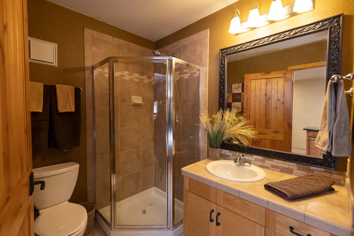 A calming ensuite bath scene with a sleek shower enclosure, a modern vanity and sink, a large mirror, and decorative greenery. The ambiance is fresh, private, and spa-like—ideal for unwinding after a long day.